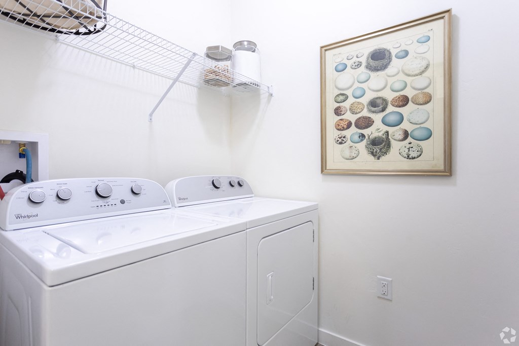 a white washer and dryer in a white laundry room with wall art at Outlook Apartments for rent in Springville and Provo, UT.
