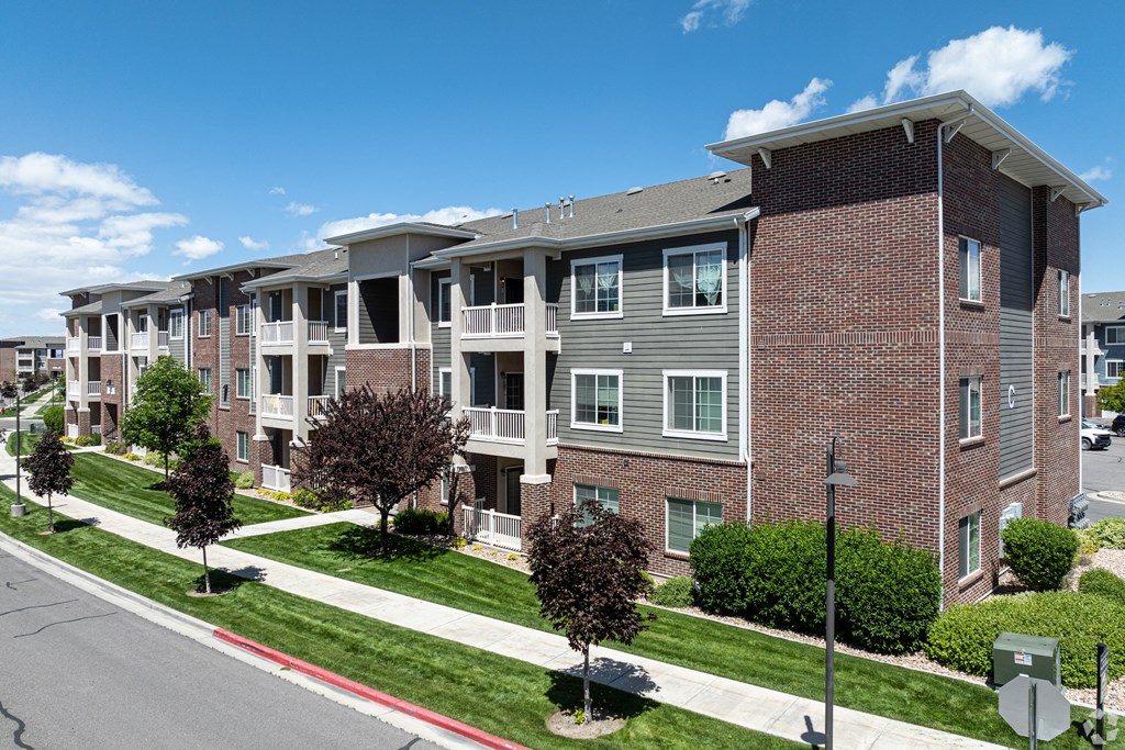an apartment building on a city street with grass and trees at Outlook Apartments for rent in Springville and Provo, UT.