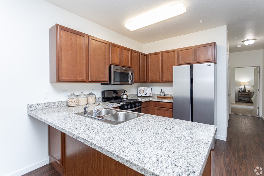 a bright kitchen with a granite counter top and a stainless steel refrigerator at Outlook Apartments for rent in Springville and Provo, UT.