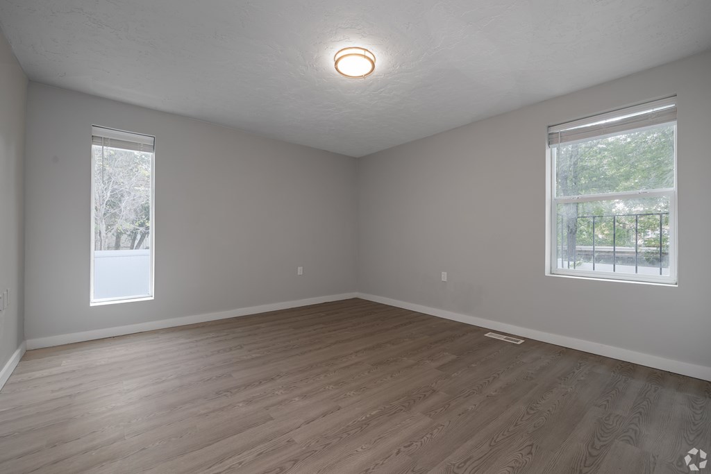 Empty room with wooden flooring and two windows.