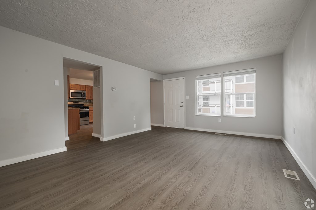A spacious empty room with wooden flooring and a doorway leading to another room.
