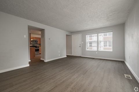A spacious empty room with wooden flooring and a doorway leading to another room.