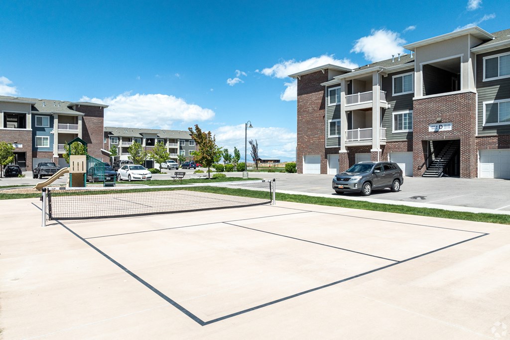 a tennis court in the middle of an apartment complex with a car parked at Outlook Apartments for rent in Springville and Provo, UT.