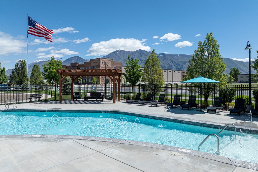 a swimming pool with a flag, fence, and mountains in the background at Outlook Apartments for rent in Springville and Provo, UT.