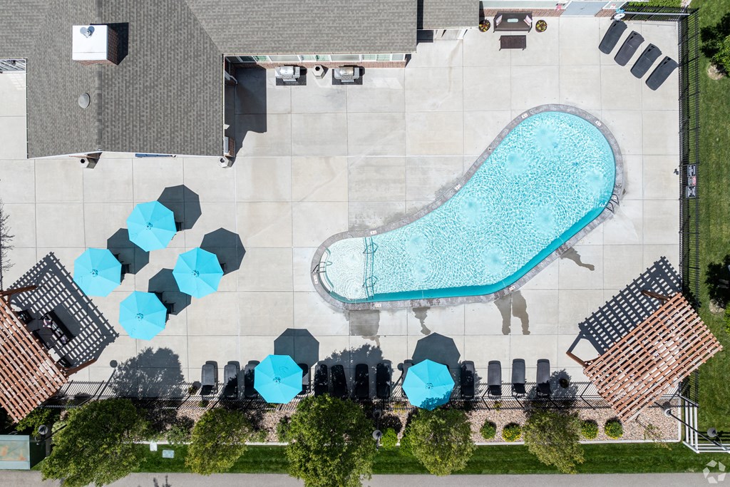 an aerial view of a pool with blue umbrellas and a poolside building at Outlook Apartments for rent in Springville and Provo, UT.