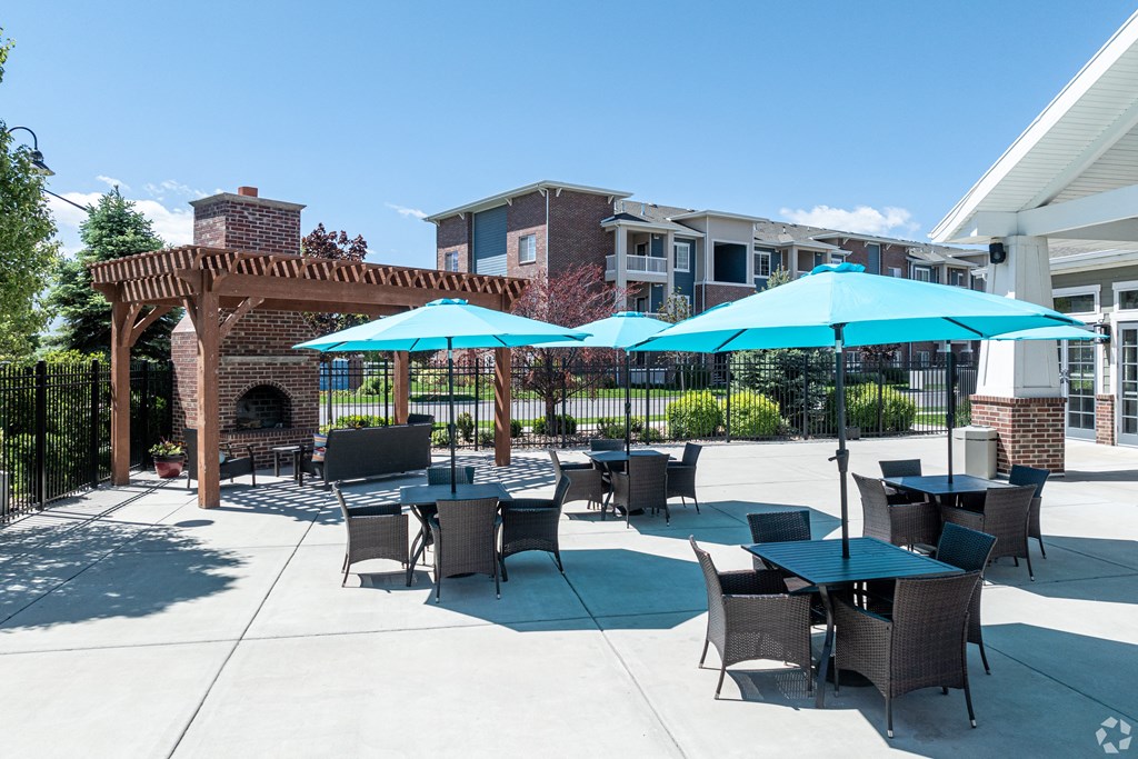 a patio with tables and umbrellas in front of a building at Outlook Apartments for rent in Springville and Provo, UT.