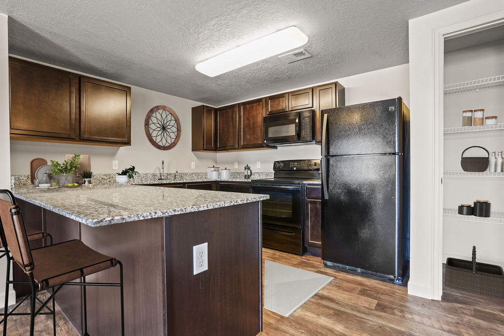 A kitchen with a black refrigerator and brown cabinets.