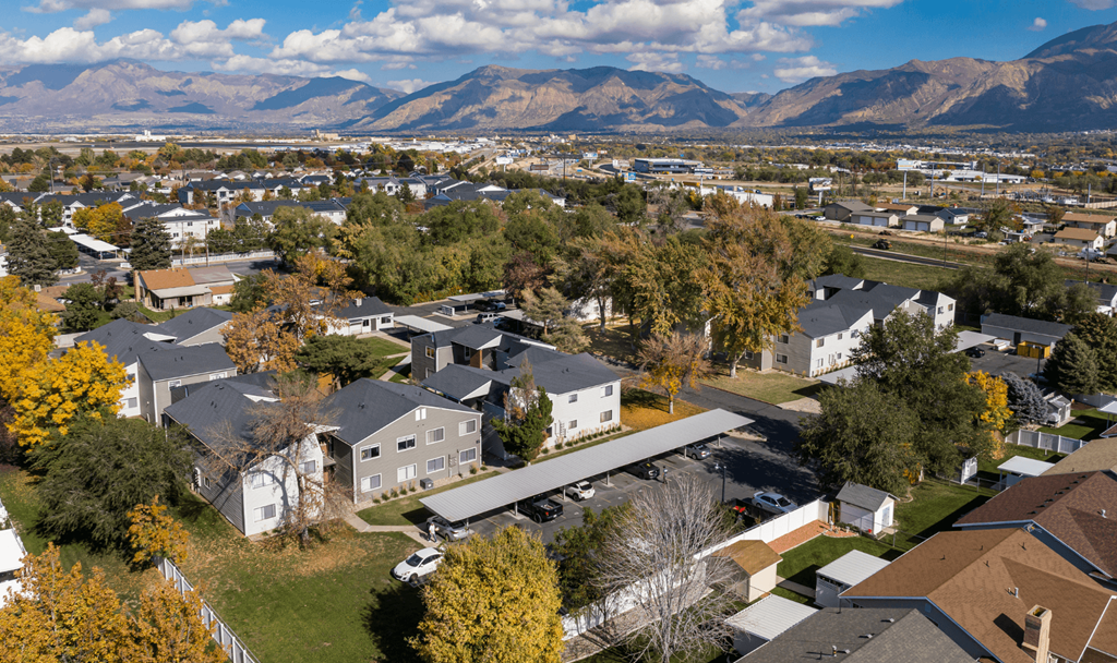 A suburban neighborhood with houses and trees in the foreground and mountains in the background.
