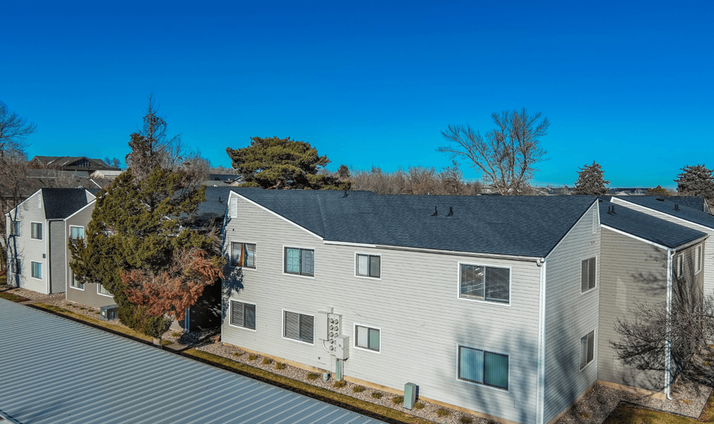 A white building with a grey roof is surrounded by trees.