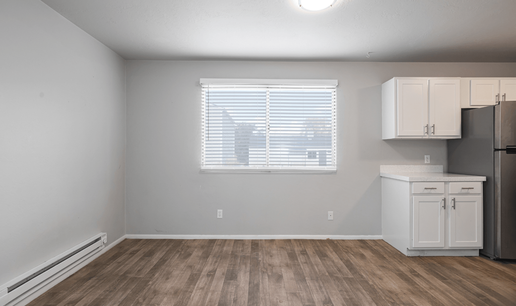 A kitchen area with a refrigerator, cabinets, and a window with blinds.