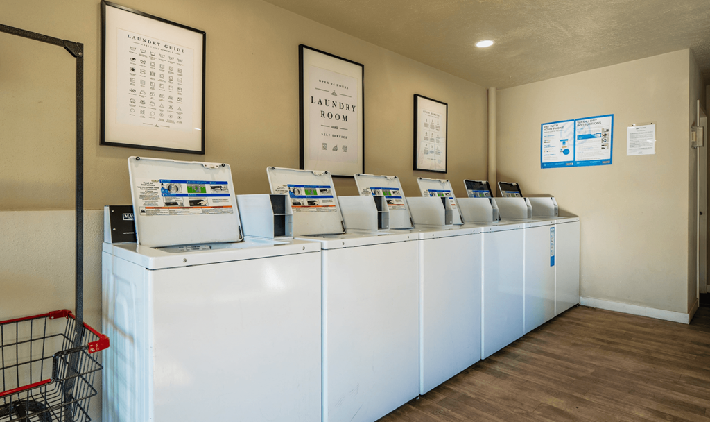 A laundry room with a row of washing machines and a shopping cart.