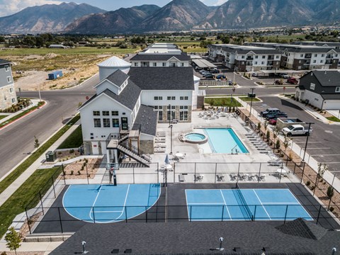 A large building with a pool and tennis court in front.