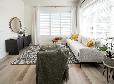 A living room with a grey sofa, a wooden table, and a mirror on the wall.