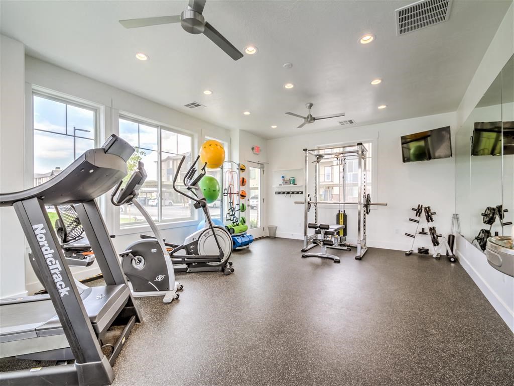 a gym with various exercise equipment and windows at Aderra apartment complex in Roy, Utah