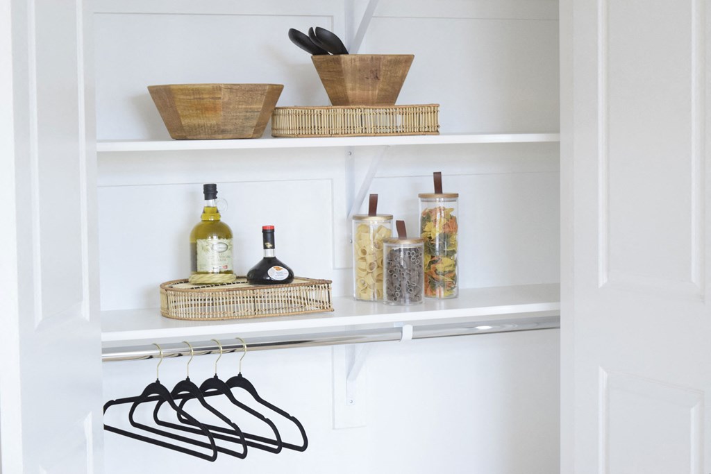 a white pantry with baskets on the top of the shelves and black hangers on the