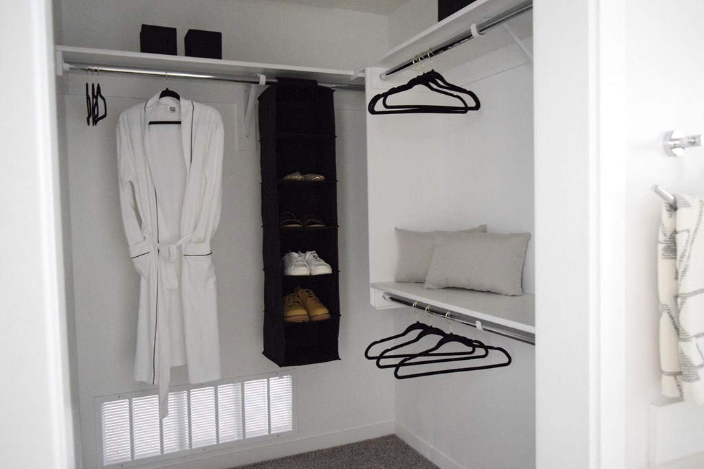 a walk in closet with a white robe and a shelf with shoes and a pillow