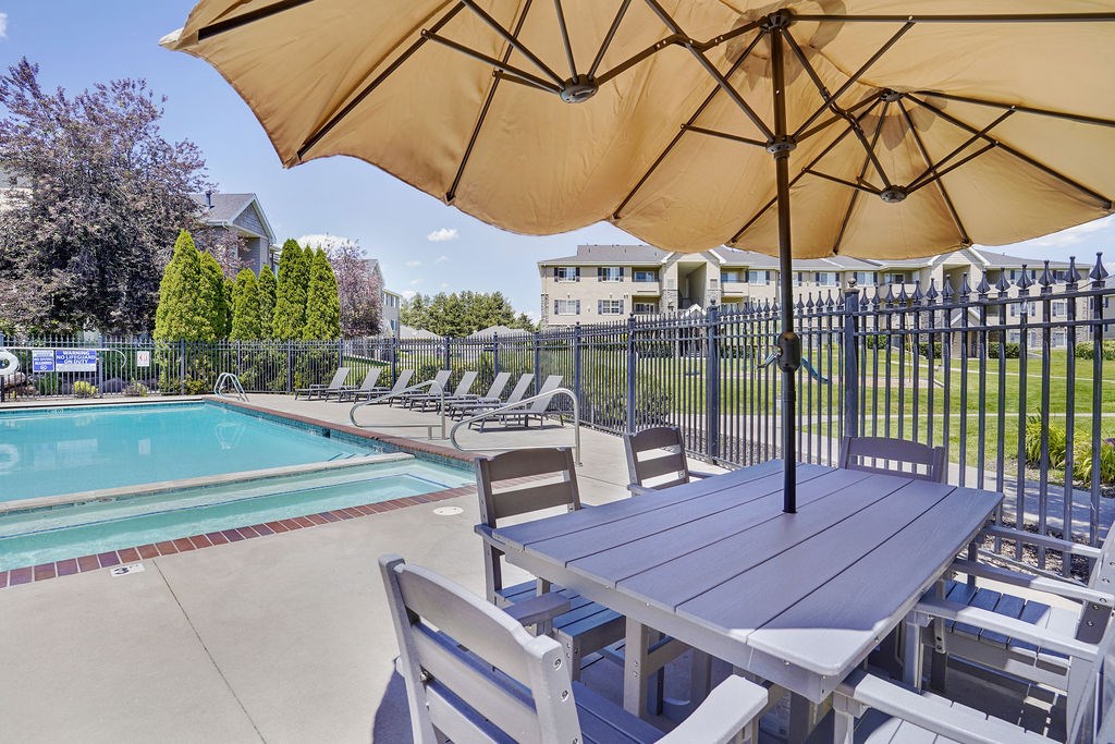 A table with chairs and an umbrella is set up by a pool.
