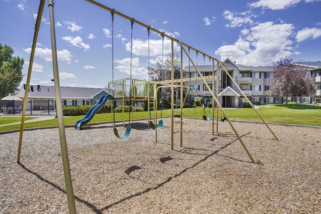A playground with swings and a slide in front of a building.