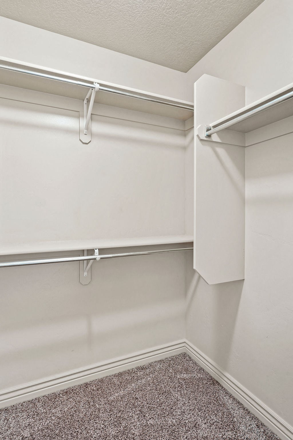 a walk in closet with a white wall and a hanging rack on the wall