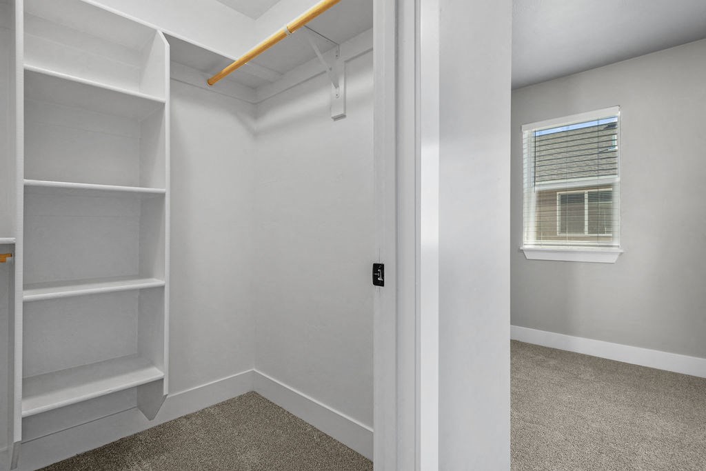the closet in a bedroom with white shelves and a window