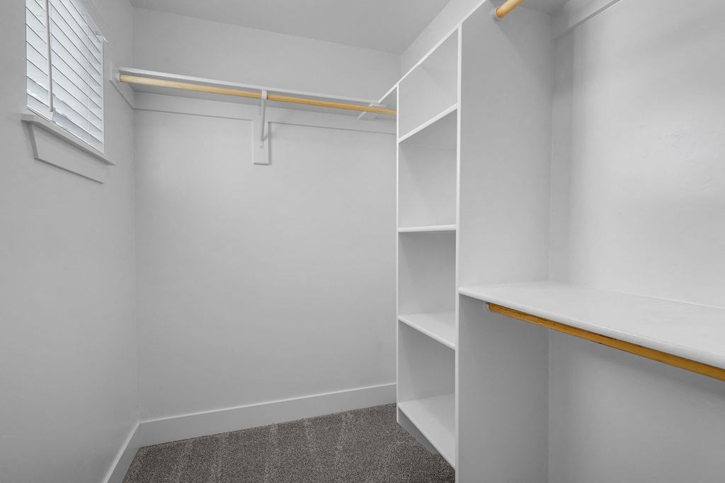 a walk in closet with white shelves and a window