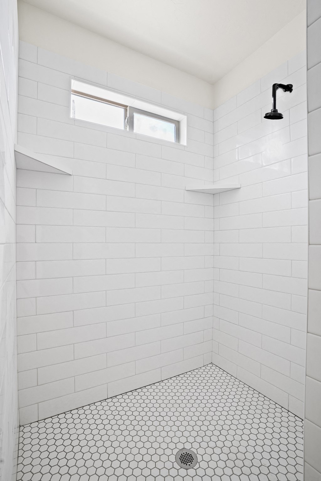 a white tiled bathroom with a shower and a window