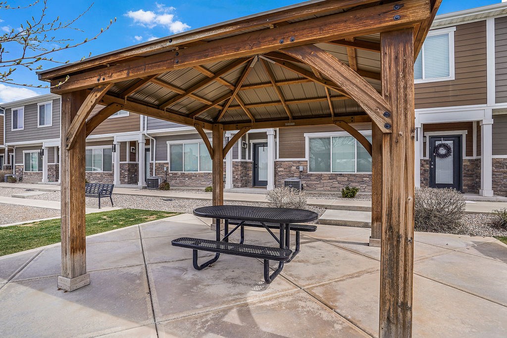 A wooden pergola with a black picnic table is in front of a building.