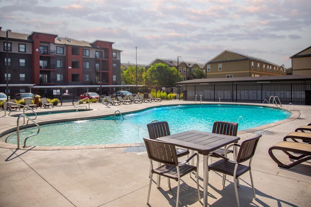 A pool with chairs and a table in front of apartment buildings.