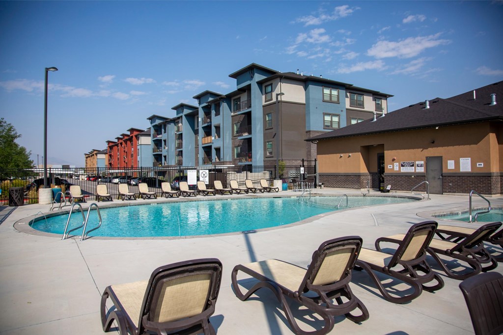 A pool with chairs around it and apartment buildings in the background.
