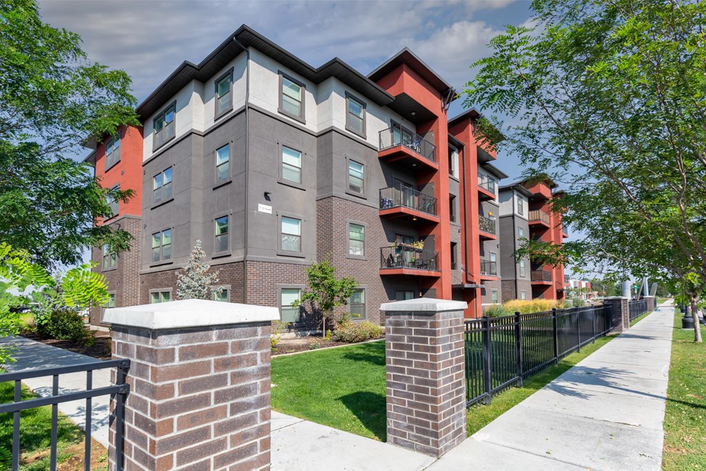 A modern apartment building with a black fence and green trees in the front.
