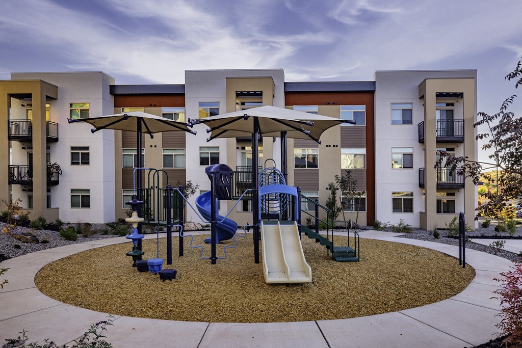 an outdoor playground with swings and umbrellas in front of apartments