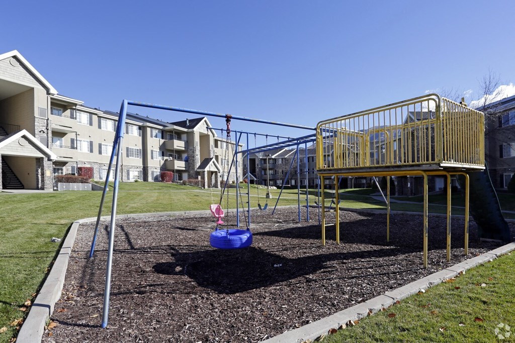 a playground with a swing set and playset in front of an apartment building