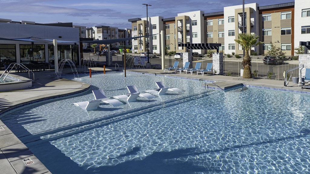a resort style pool with white lounge chairs in it with an apartment building behind it