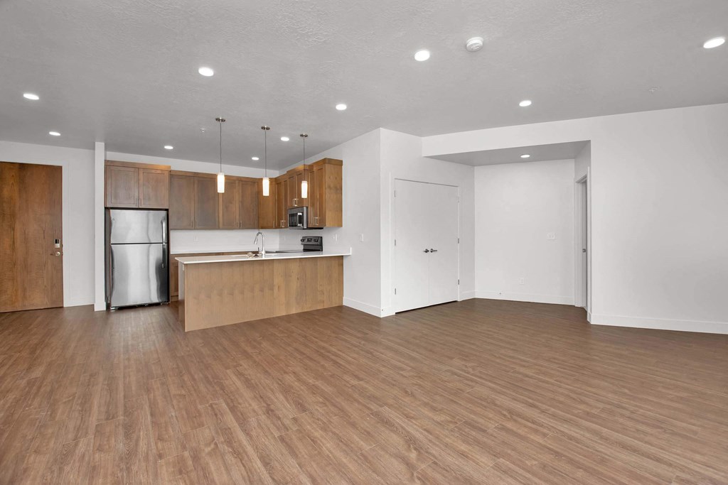 an empty living room with a kitchen in the background