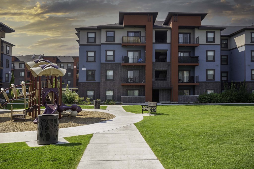 a pathway leading to an apartment building with a playground in the foreground