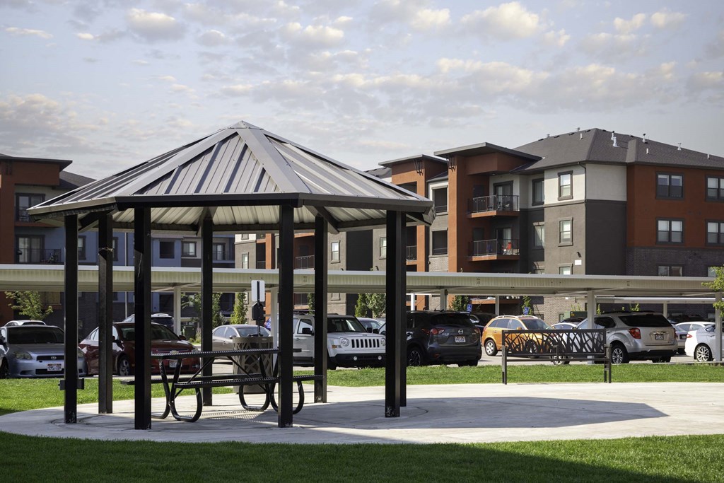 a gazebo in a park with apartment buildings in the background