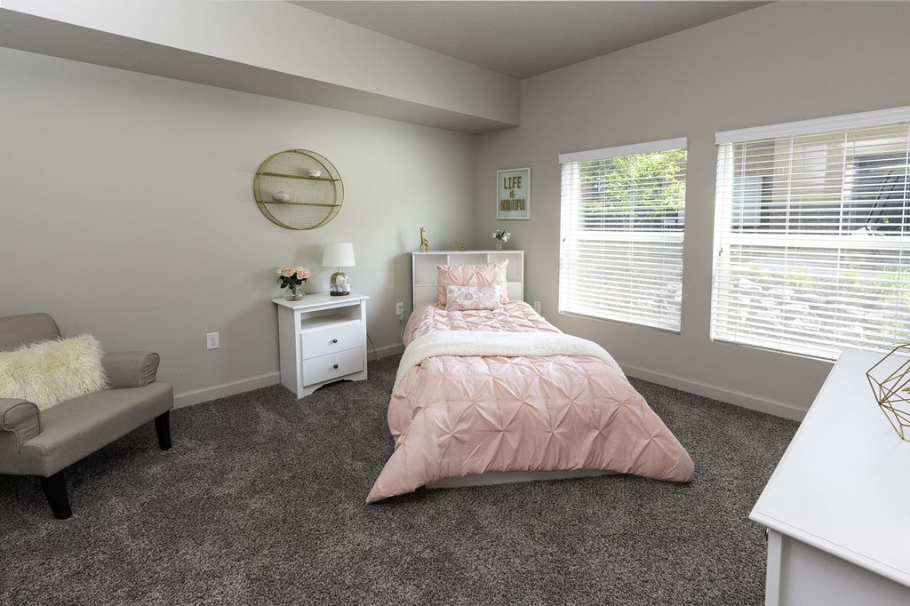 a bedroom with gray carpeting and a bed with a pink comforter