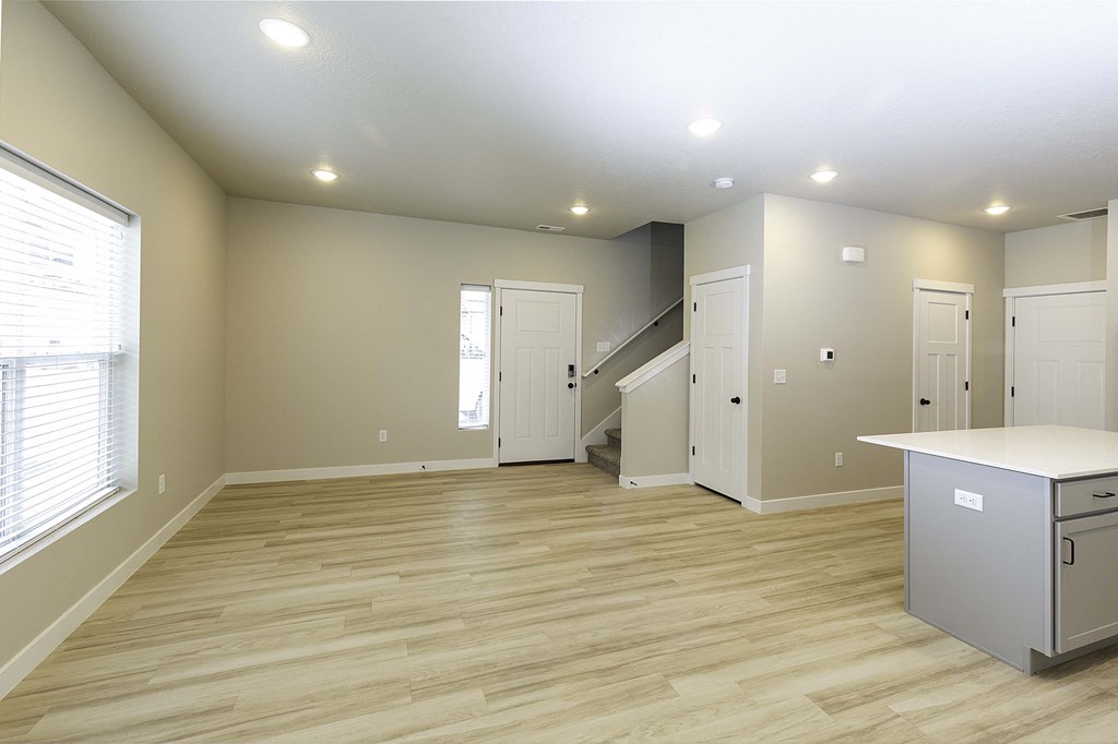an empty living room with a staircase in the background and a kitchen in the foreground