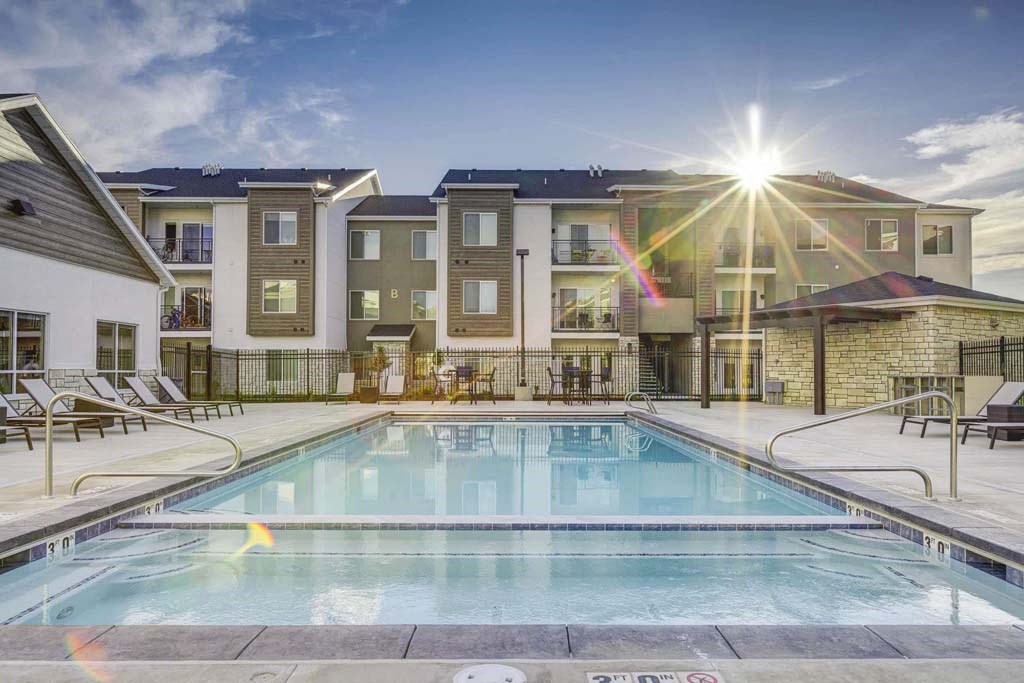 A swimming pool in front of a building with sunlight shining through the clouds.