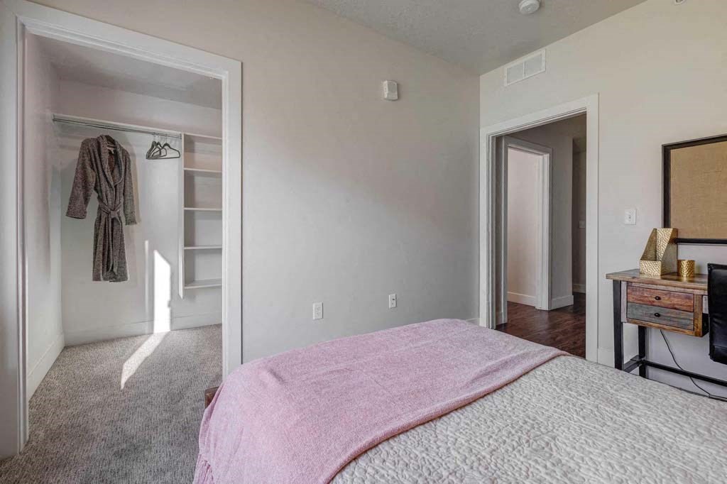 A bedroom with a pink bedspread and a wooden dresser.
