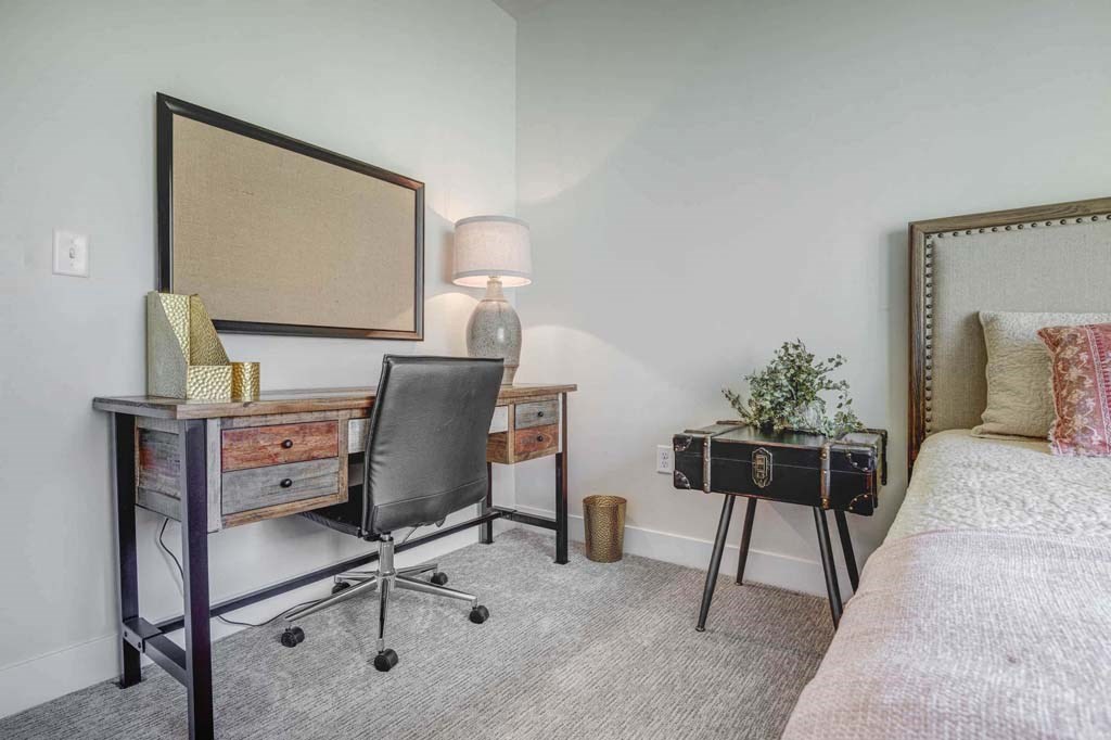 A bedroom with a bed, desk, chair, and lamp.