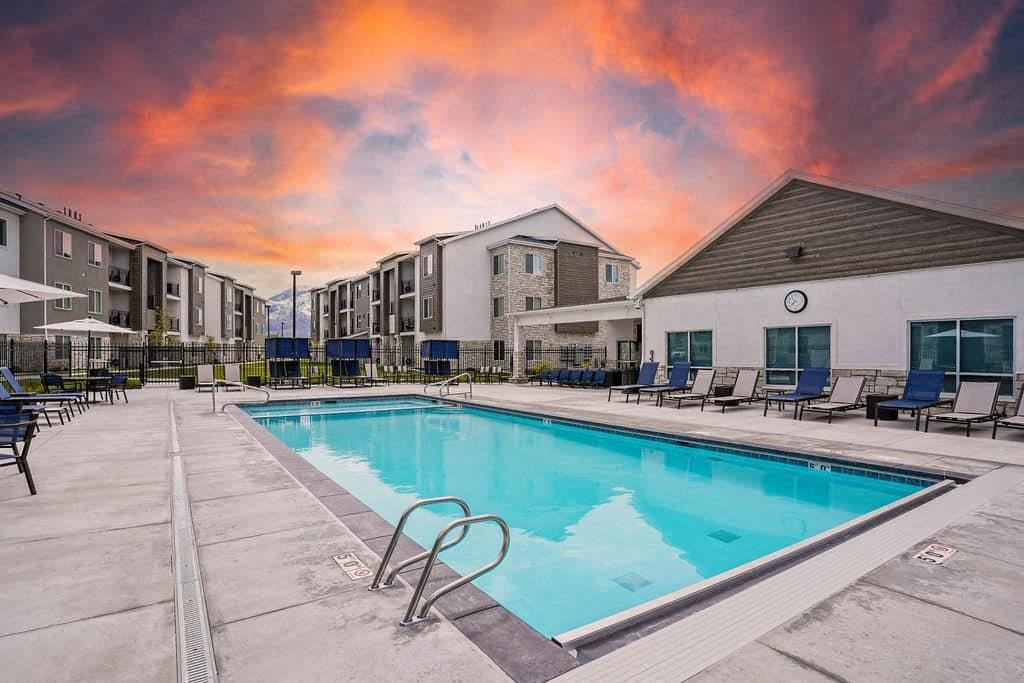 A swimming pool surrounded by lounge chairs and apartment buildings.