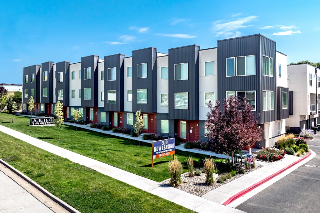 A row of modern townhouses with a "For Sale" sign in front.