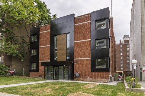 A modern brick building with black windows and a green lawn in front.