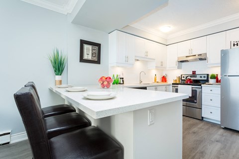 A white kitchen with a black chair and a fridge.