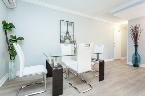 A dining room with a glass table and white chairs.