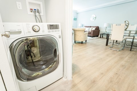 A white front loading washing machine in a room with a wooden floor.