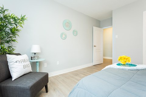 A bedroom with a grey bedspread and a grey couch with a pillow that says "BIG".