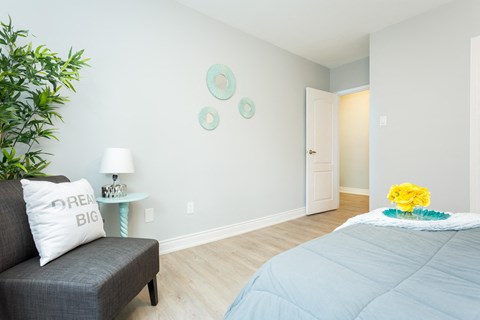 A bedroom with a grey bedspread and a grey couch with a pillow that says "BIG".