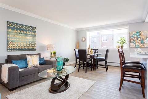 A living room with a grey couch, a glass coffee table, and a dining table with chairs.